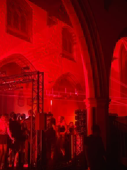 An image of a nightclub event inside a church hall lit with red lighting and stage equipment.