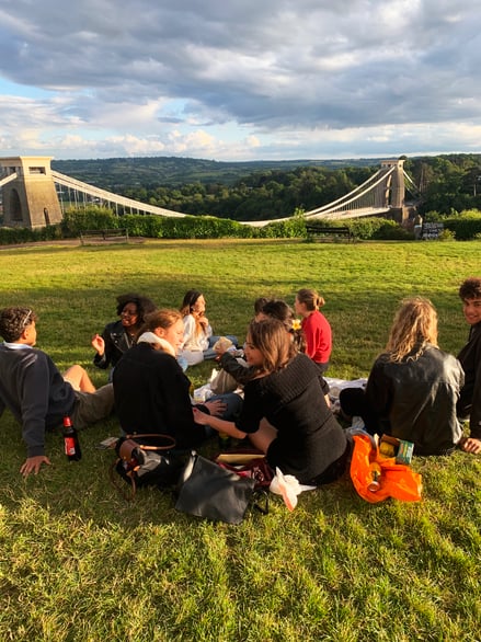 Group of students sitting on grass with Clifton Suspension Bridge in background