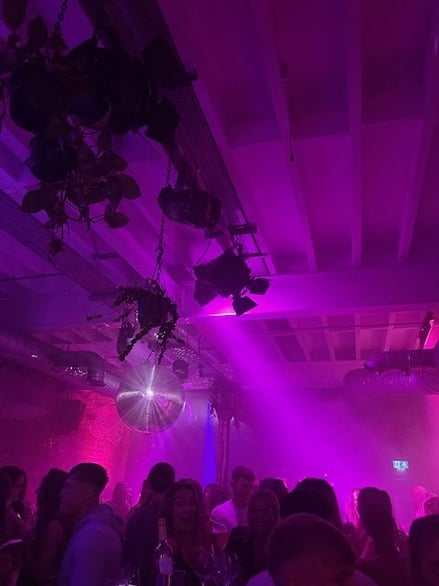 Crowded nightclub with purple lighting, disco ball, and people socialising in Leeds