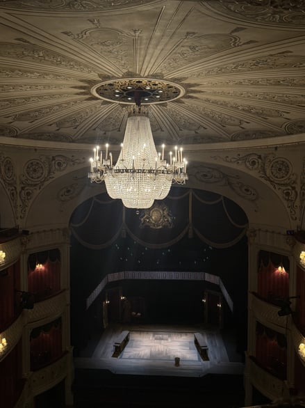 View of theatre stage beneath ornate ceiling and large chandelier