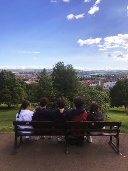 Friends sitting on bench overlooking Bristol city skyline from park