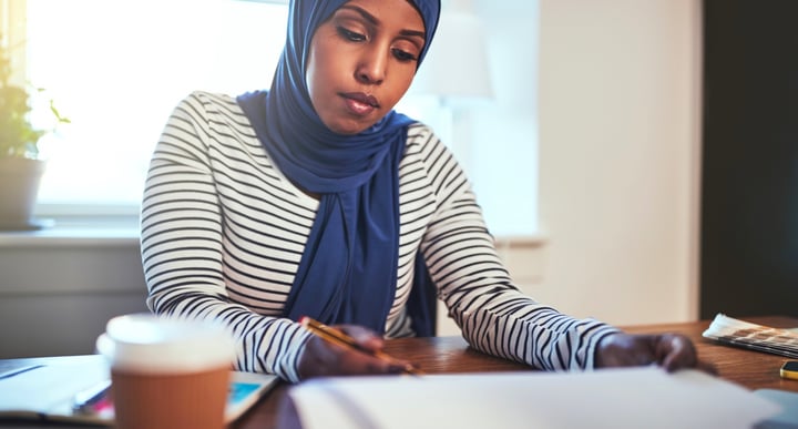A woman in headscarf is sat at a desk looking over documents
