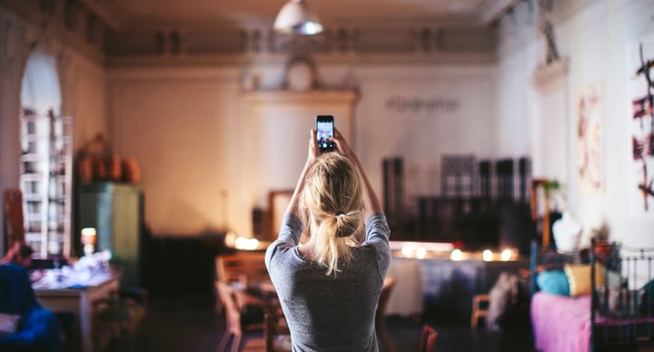 A female student is holding a mobile phone up high, taking a photo of a dining room space